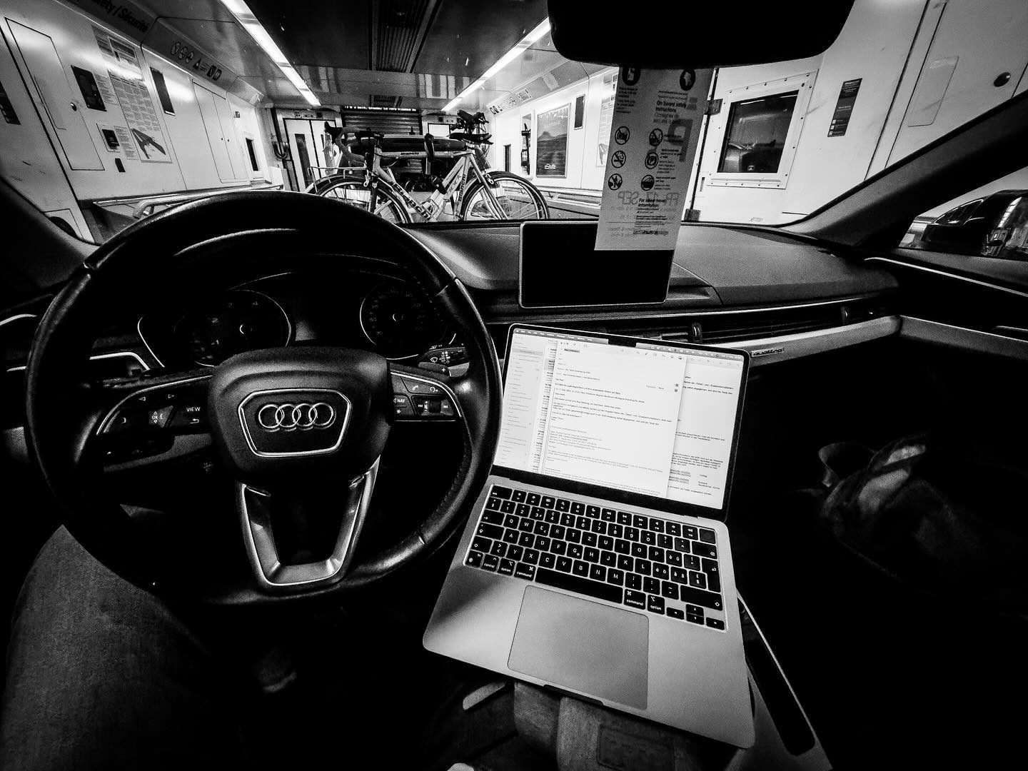 Black and white photo of an open laptop inside a car which is travelling inside a train of the Eurotunnel