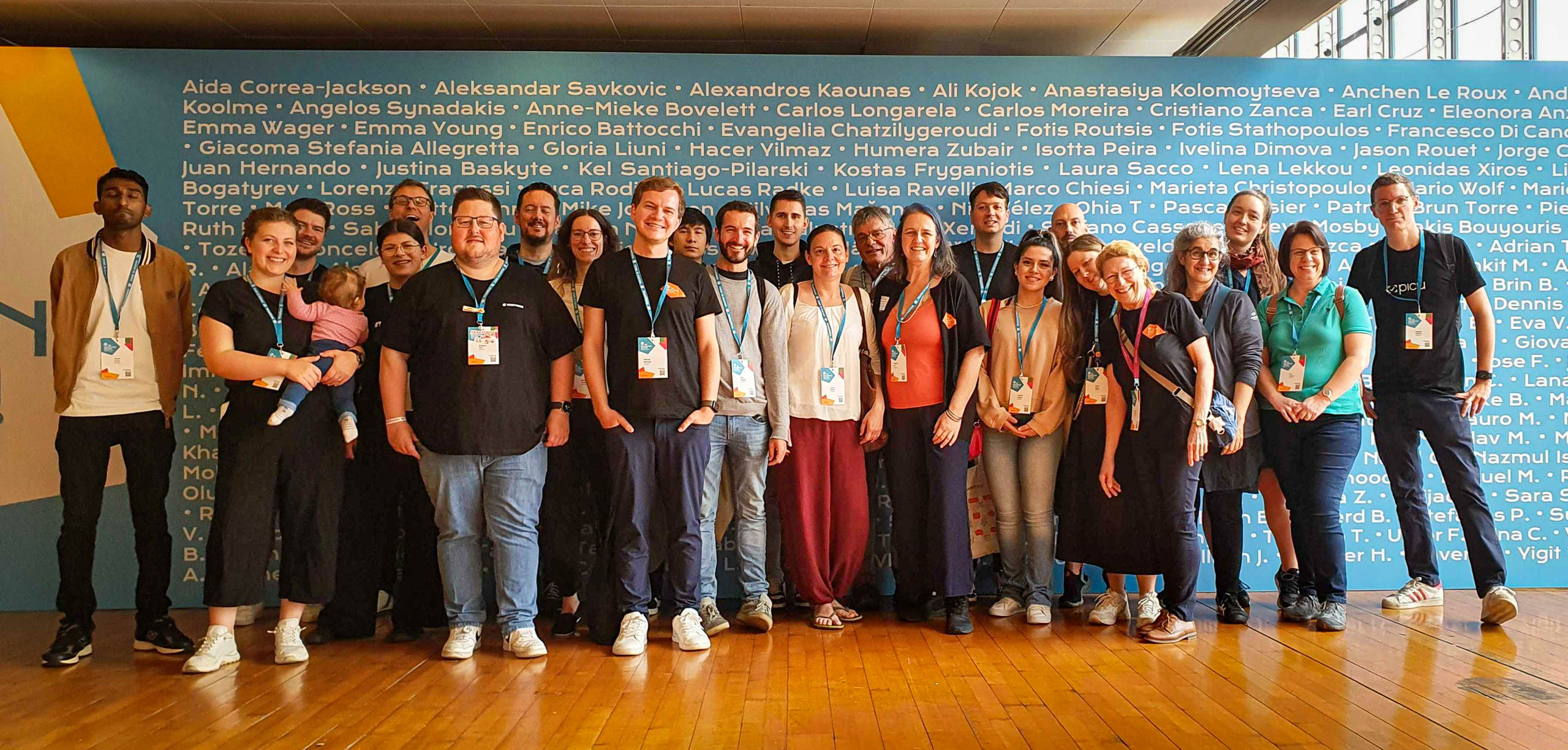 A group of friends and colleagues pose in front of a background covered with names at WordCamp Europe in Turin, 2024